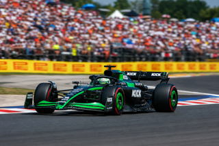 (A high-detail Formula 1 race car attacking a tight sequence of corners at the Hungaroring, summer sunlight, packed grandstands, heat haze over the asphalt, dynamic panning shot, motorsport photography, 400mm lens feel, crisp sponsor detail, energetic but realistic race atmosphere