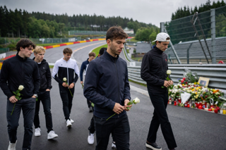 Pierre Gasly and drivers walking quietly along Spa-Francorchamps toward the memorial area at Raidillon, overcast Belgian summer light, respectful atmosphere, cinematic sports documentary style