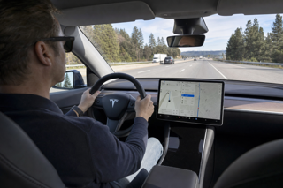 Realistic in-car shot of a driver gently applying slight turning force to a Tesla steering wheel during highway driving, road visible ahead, calm focused posture, natural daylight, documentary automotive photography, premium clarity