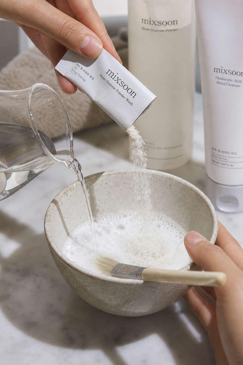 close-up skincare routine scene, hand pouring fine enzyme powder into a ceramic bowl, adding water with brush to create dense foam, soft side lighting, visible creamy clay texture, clean bathroom editorial style, realistic skin care process photography