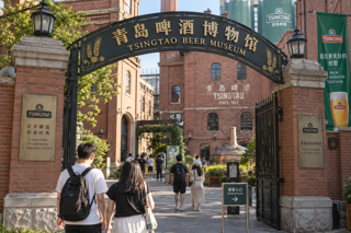 Photorealistic travel editorial photo of Tsingtao Beer Museum red brick entrance in Qingdao, late afternoon natural light, clear signage, people walking naturally, 35mm lens, documentary style