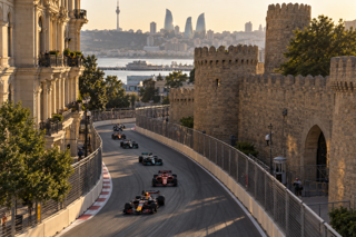 Aerial telephoto photograph of Baku City Circuit running between modern city streets and the old town walls, late afternoon sunlight, realistic motorsport atmosphere, long lens compression, crisp asphalt texture, natural shadows, no text overlay